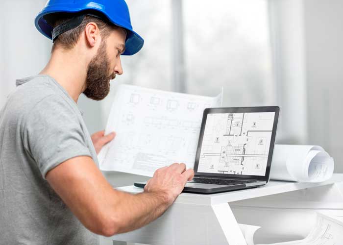 csi-remote-work a photograph of a male in a blue hard hat working on a computer.