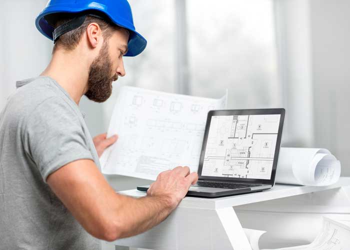 a photograph of a male in a blue hard hat working on a computer.